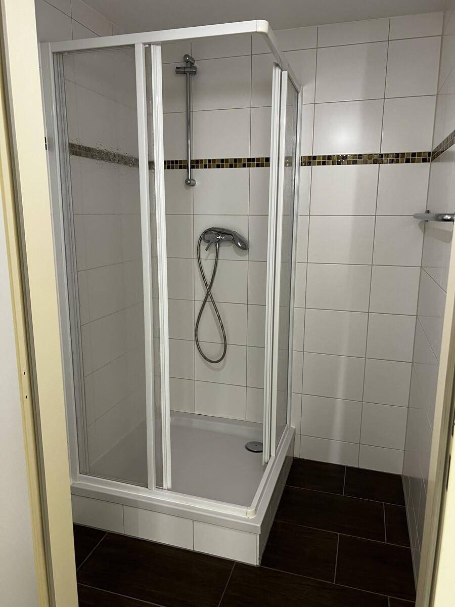 Duschkabine in einem gefliesten Badezimmer mit weißer Wand und dunklem Boden.