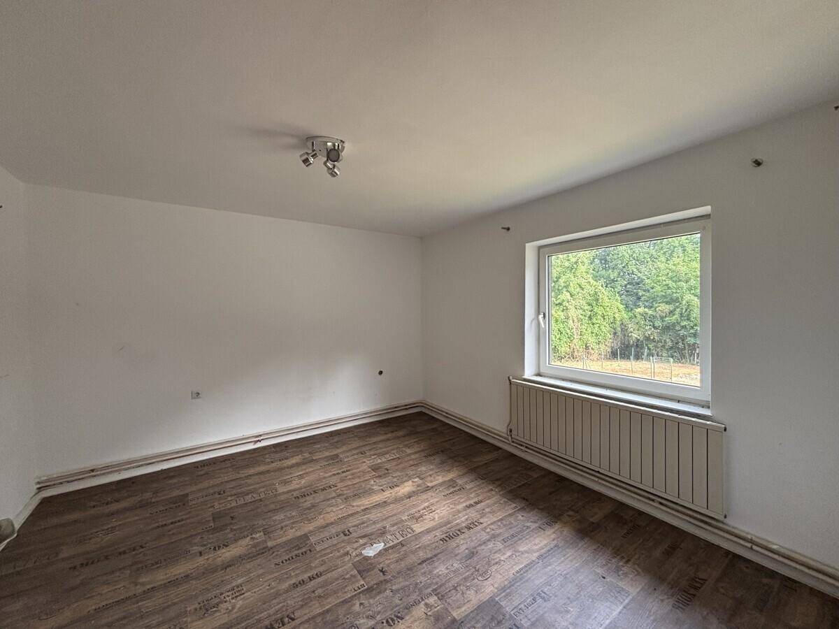 Geräumiges Schlafzimmer mit Laminatboden, weißen Wänden und großem Fenster zum Garten.