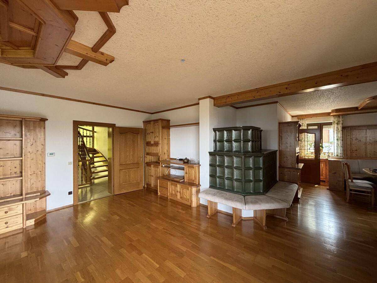 Gemütliches Wohnzimmer mit traditionellem Kachelofen, Holzeinbauten und Zugang zum Treppenhaus.