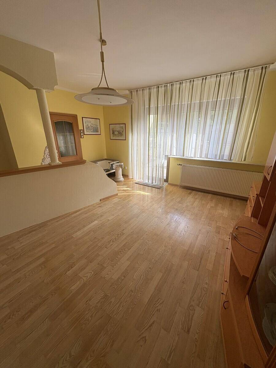 Heller Wohnbereich mit großen Fenstern, Holzboden und gelben Wänden.