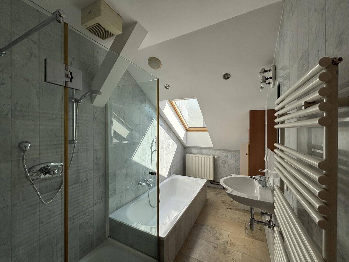 Gefliestes Badezimmer im Dachgeschoss mit Badewanne, Dusche, Waschbecken und beheiztem Handtuchhalter.
