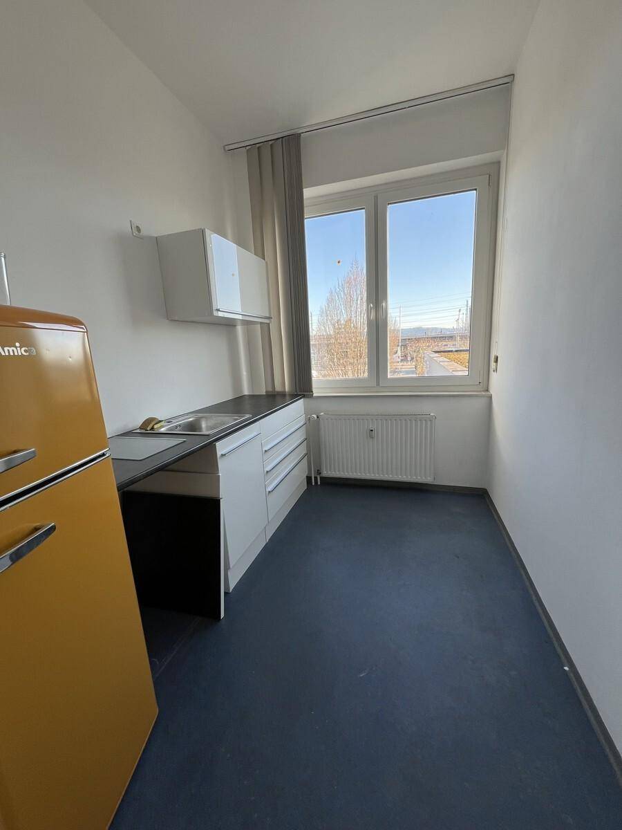 Kleine Küchenzeile mit gelbem Retro-Kühlschrank, weißen Schränken und Fenster.