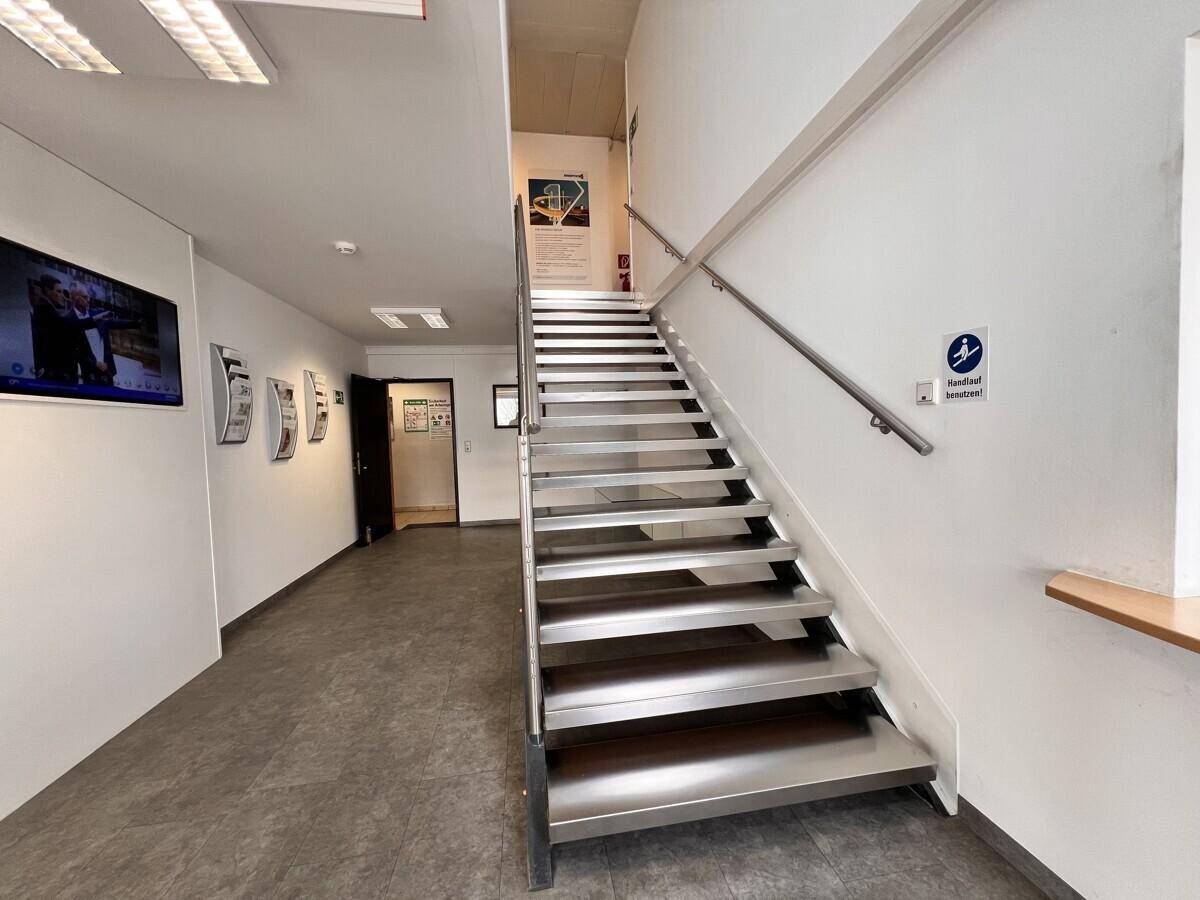 Eingangsbereich mit einer modernen Metalltreppe und Handlauf, die zu den oberen Etagen führt.