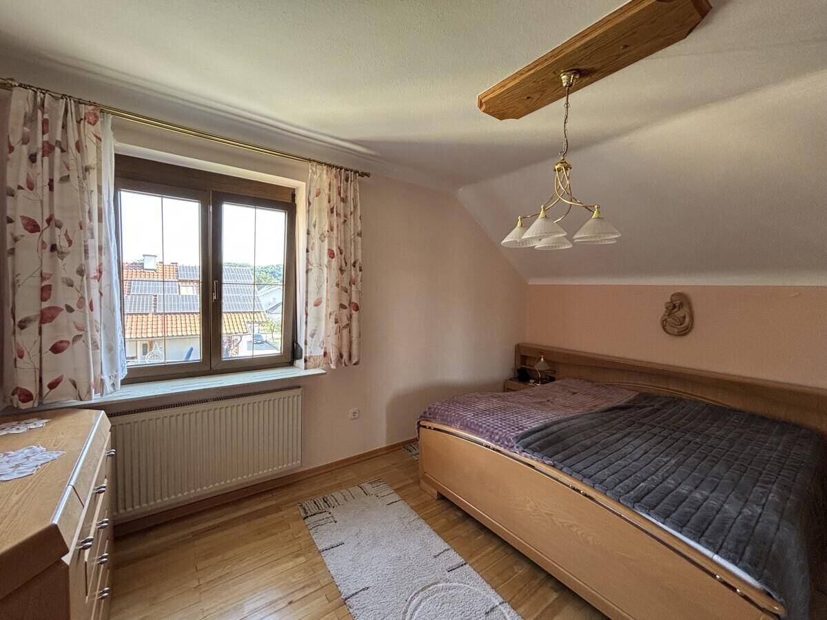 Helles Schlafzimmer mit Doppelbett, Holzboden und Fenster mit Blick nach draußen.