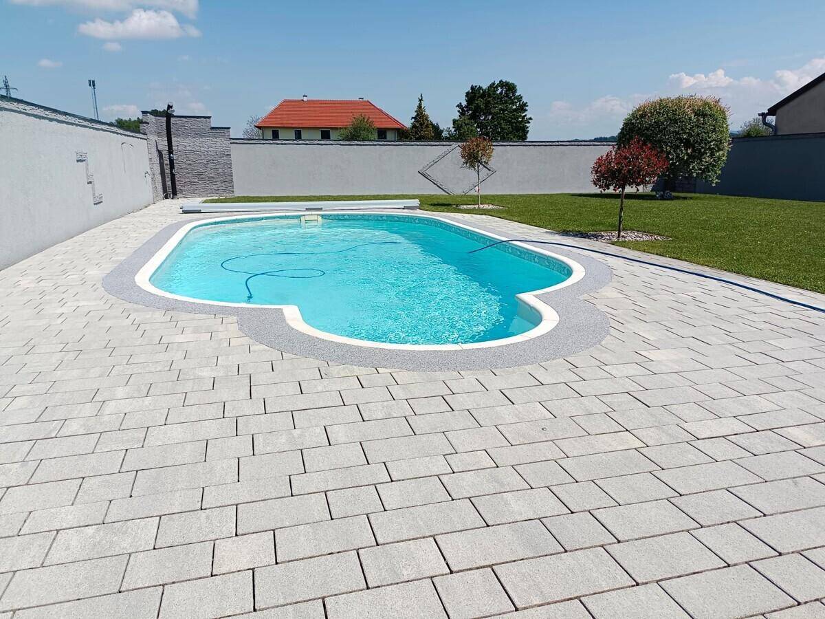 Großzügiger Poolbereich mit gepflasterter Terrasse und Rasenfläche im sonnigen Garten.
