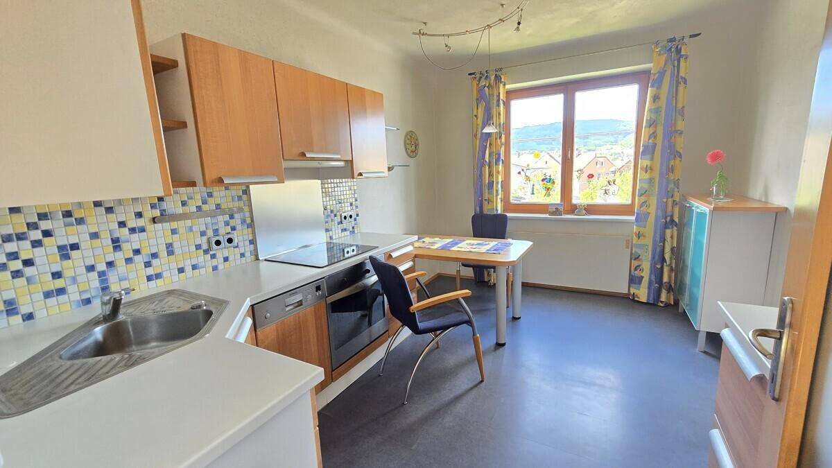 Helle Küche mit Essbereich, blauen Fliesen, modernen Geräten und einem Fenster mit Ausblick.