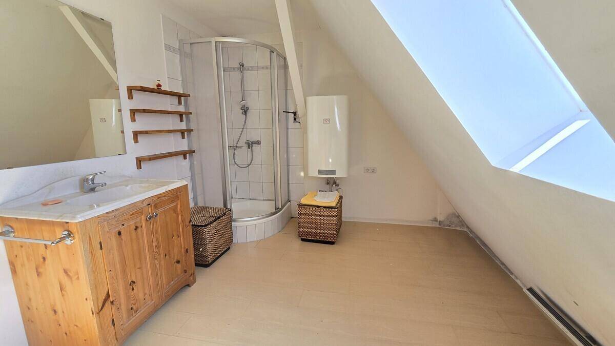Badezimmer im Dachgeschoss mit Dachfenster, Dusche, rustikalem Holzwaschtisch und hellem Boden.