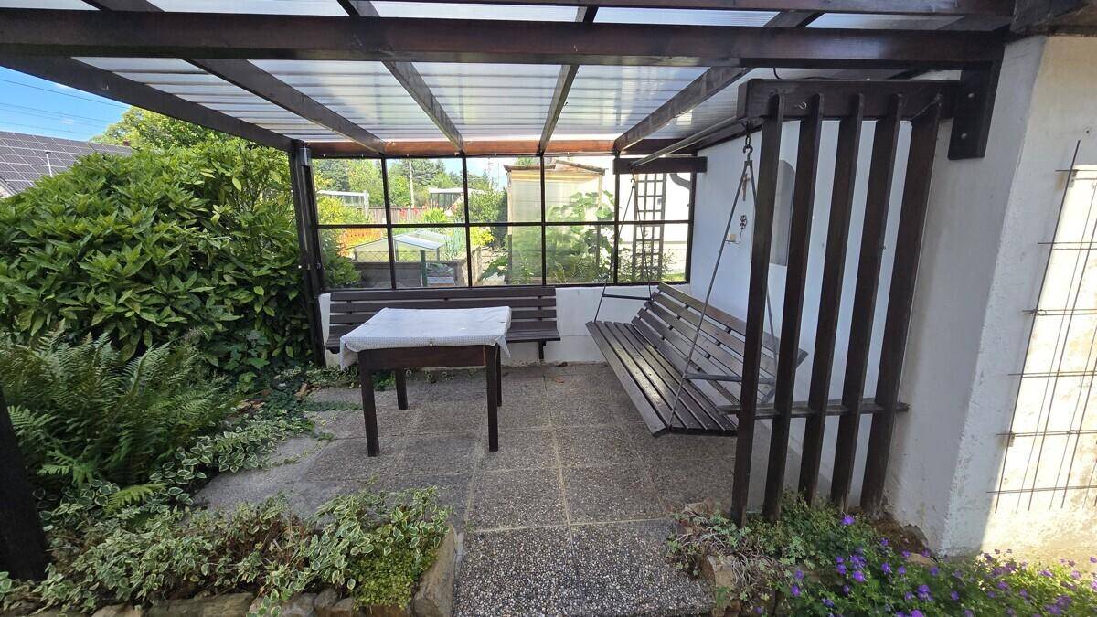 Überdachter Sitzbereich im Freien mit Holzbänken und Blick auf den Garten.