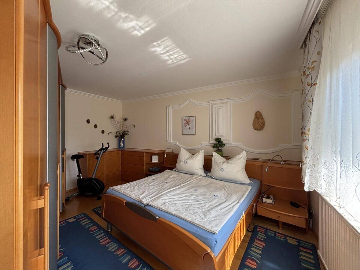 Schlafzimmer mit Doppelbett, Holzmöbeln und Stuckverzierungen an der Wand.