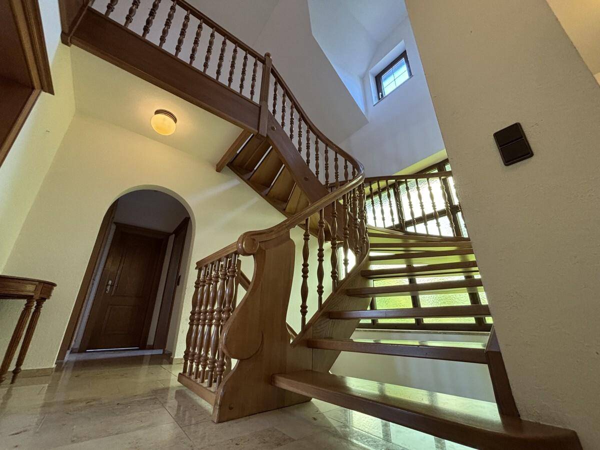 Elegante Holztreppe mit gedrechselten Geländerstäben und hellem Marmorboden im Eingangsbereich.