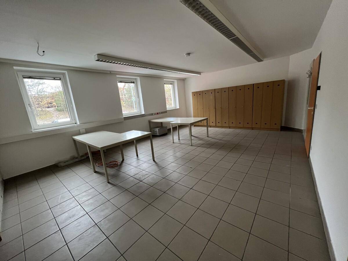Heller Büroraum mit zwei Tischen, Fliesenboden und einer Reihe von Holzschränken entlang der Wand.