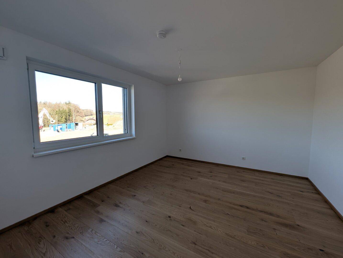 Ruhiges Schlafzimmer mit hellem Eichenparkett und einem großen Fenster, das viel Tageslicht hereinlässt.