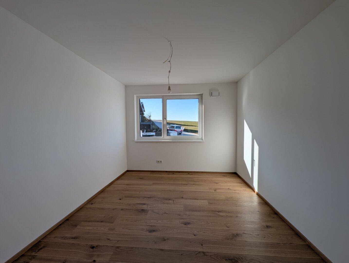 Helles Schlafzimmer mit Eichenparkettboden und einem Fenster, das einen weiten Blick in die Landschaft bietet.