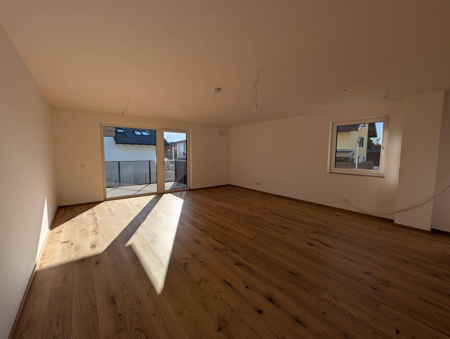 Geräumiger, heller Wohnbereich mit Eichenparkettboden und Zugang zu einem Balkon, durchflutet von Sonnenlicht.