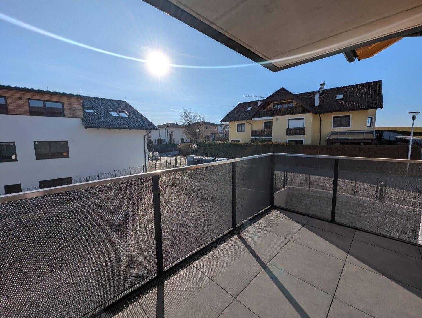 Sonniger Balkon mit Fliesenboden und modernem Metallgeländer, bietet einen Blick auf die Nachbarschaft.