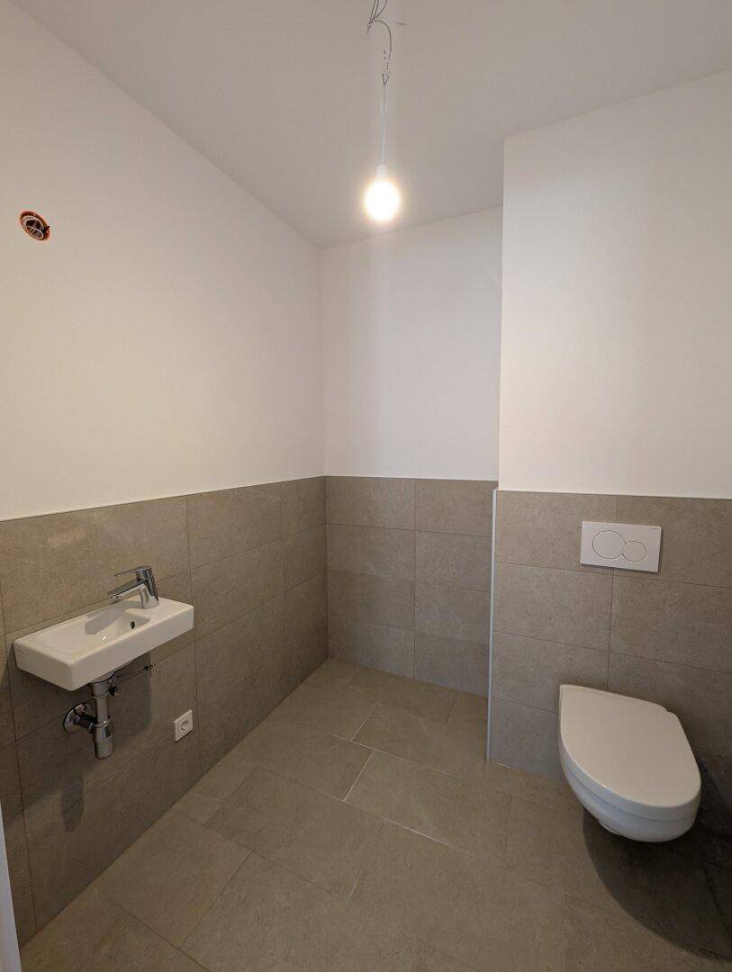 Praktisches Gäste-WC mit modernen grauen Fliesen, wandhängendem WC und einem kleinen Waschbecken.