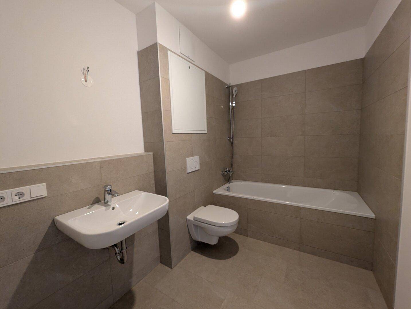 Modernes Badezimmer mit Badewanne, Wand-WC und großformatigen grauen Fliesen.