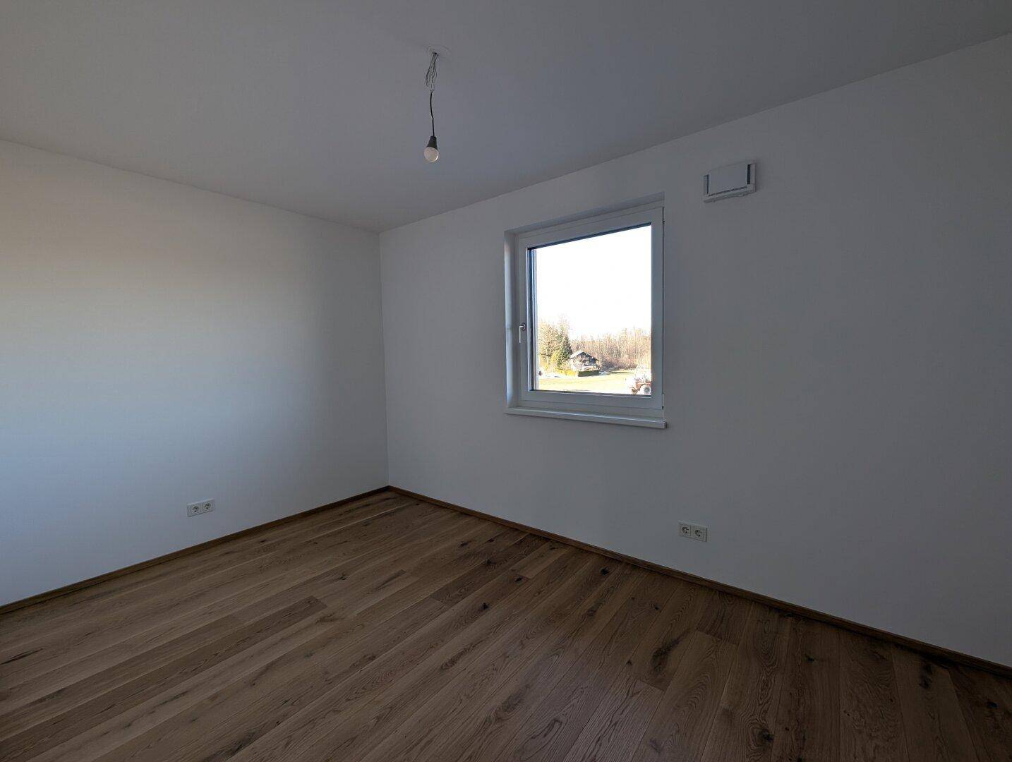 Ruhiges Schlafzimmer mit Eichenparkett und einem Fenster, das viel Tageslicht hereinlässt.
