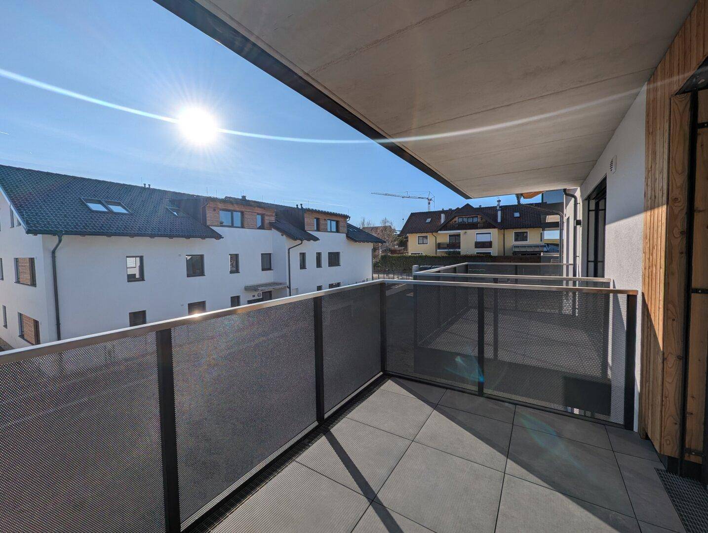 Sonniger Balkon mit Fliesenboden und Blick auf die umliegenden Wohngebäude und den blauen Himmel.