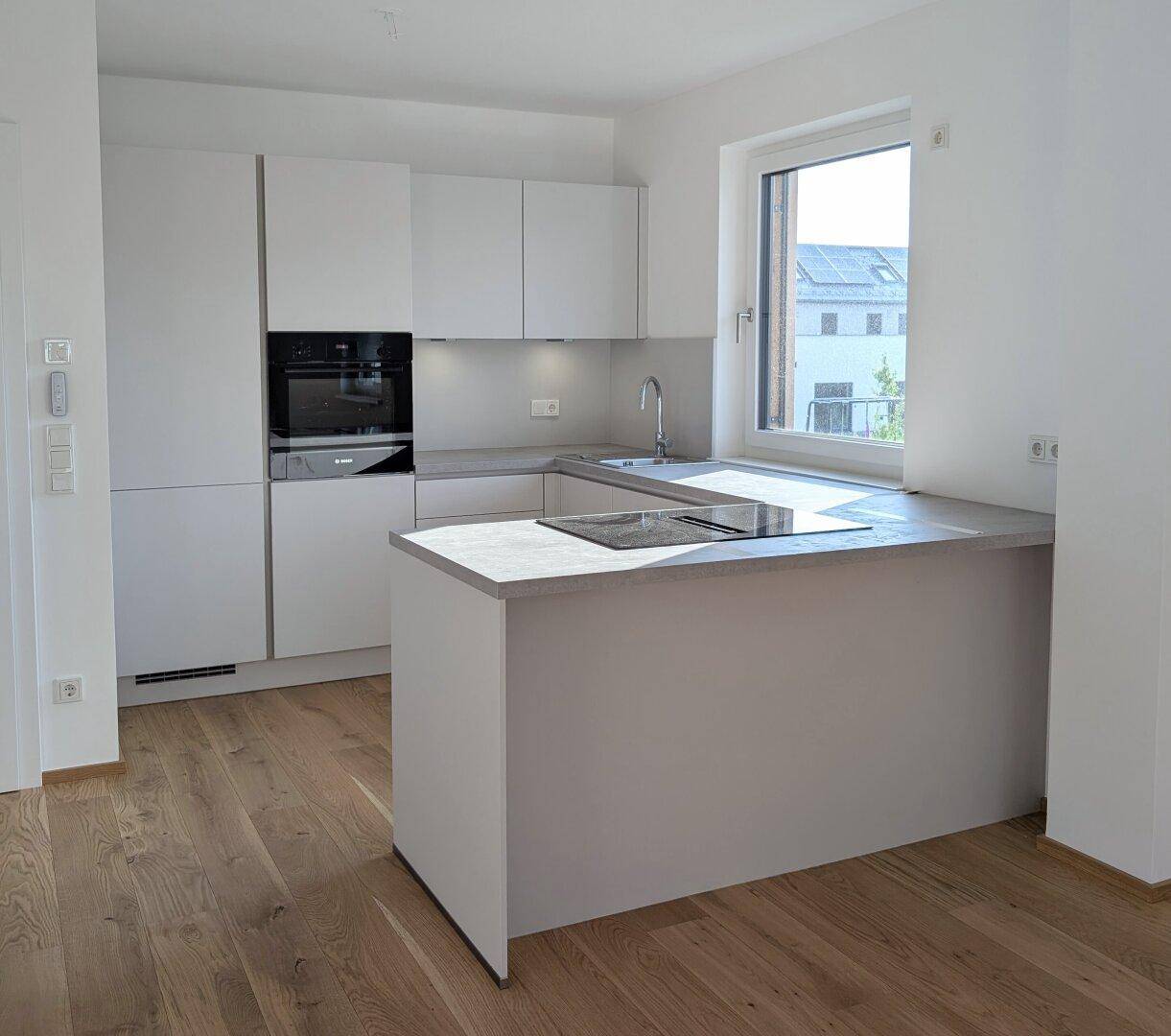 Moderne Einbauküche mit hellgrauen Fronten, Induktionskochfeld und Holzparkettboden.