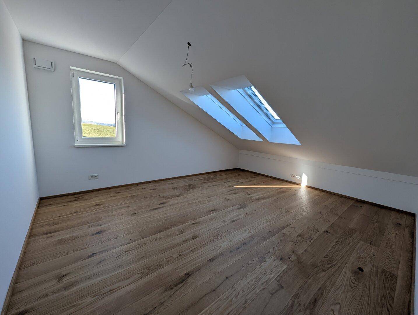 Heller Raum mit Holzboden, Dachschrägen und Dachfenstern, ideal als Schlaf- oder Arbeitszimmer.