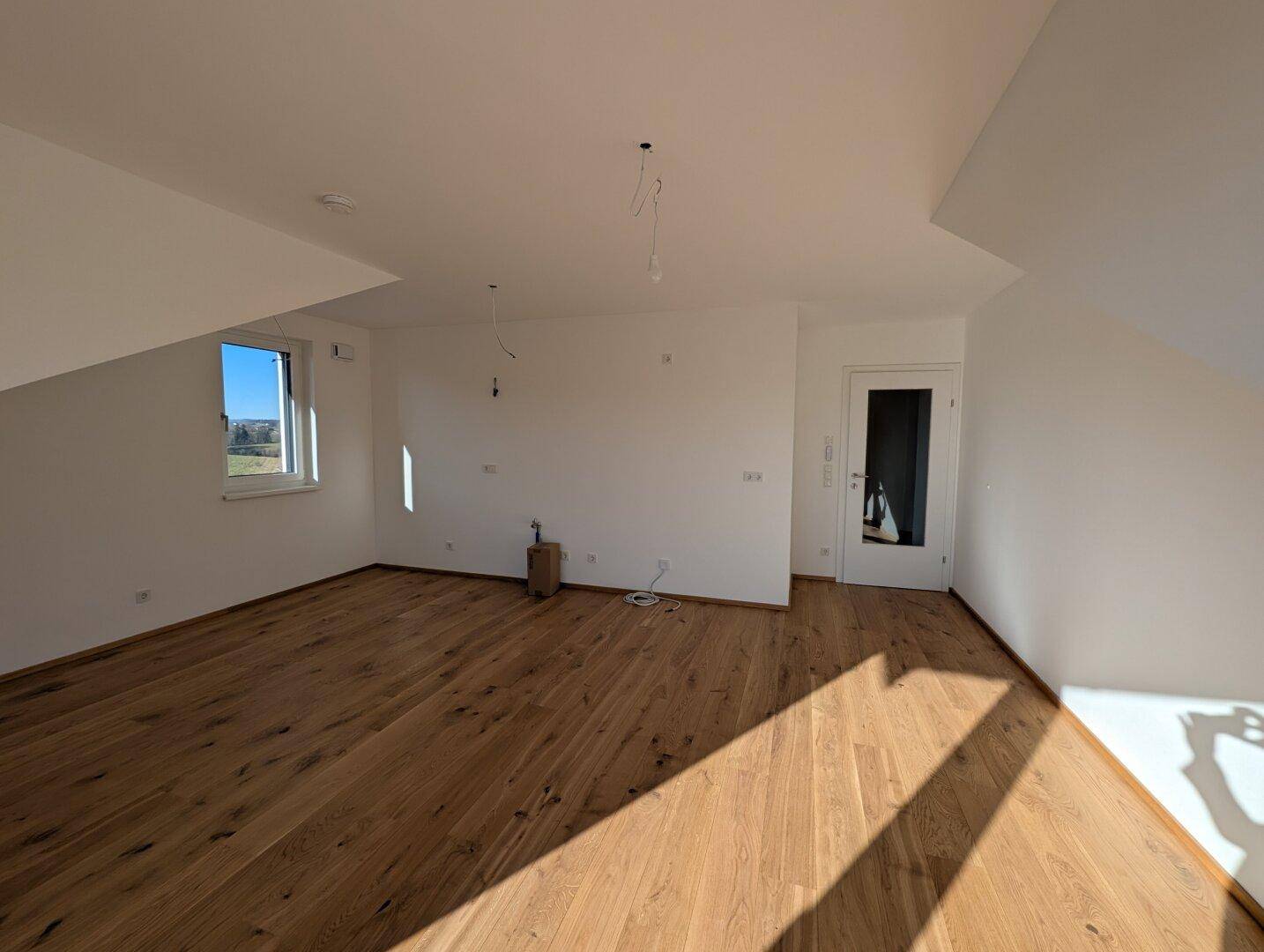 Geräumiger, heller Raum mit Holzboden und Dachschrägen, ideal als Wohn- oder Schlafzimmer.