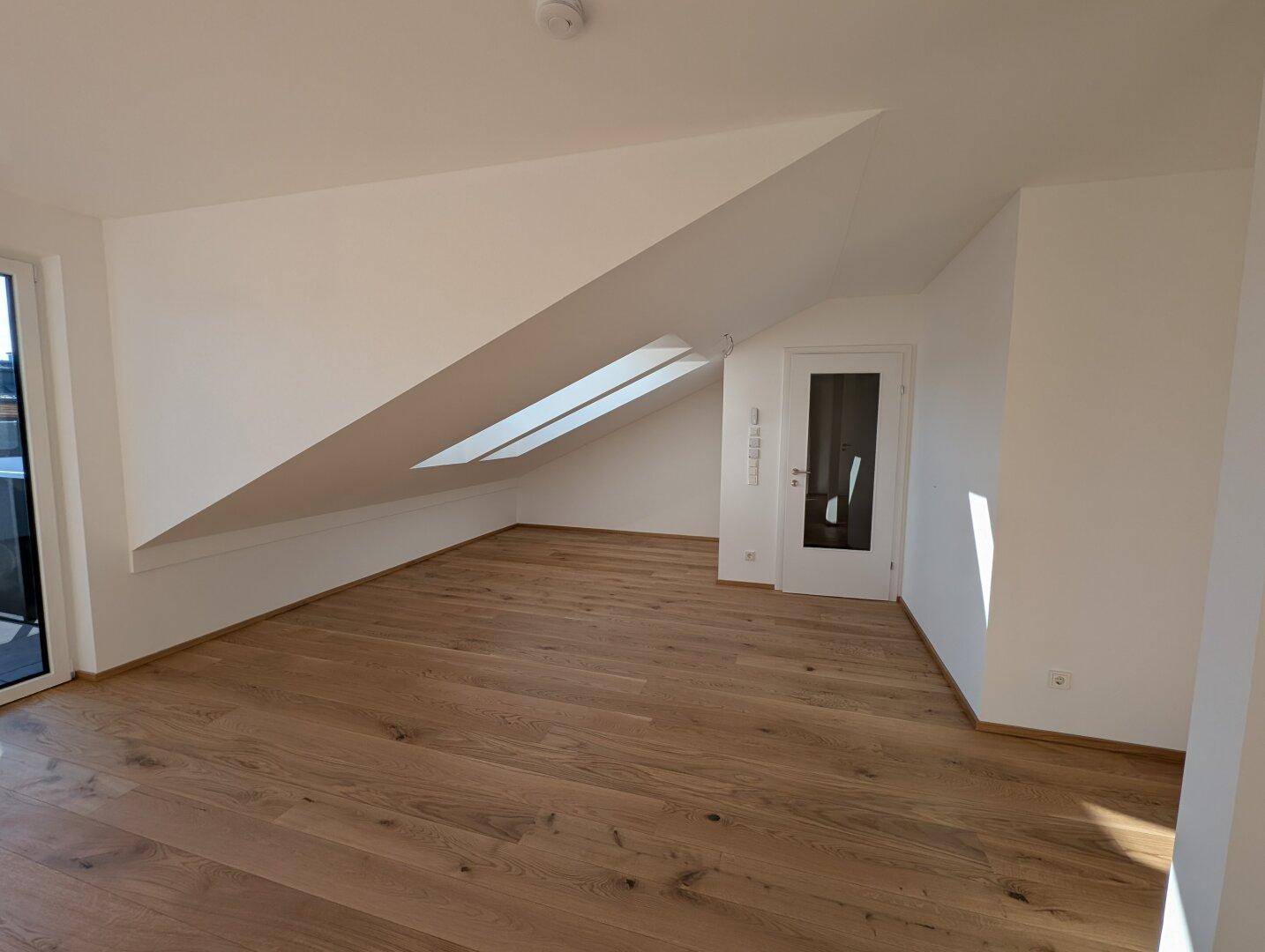 Lichtdurchfluteter Raum im Dachgeschoss mit Holzboden und Dachfenster, ideal als Schlaf- oder Wohnbereich.