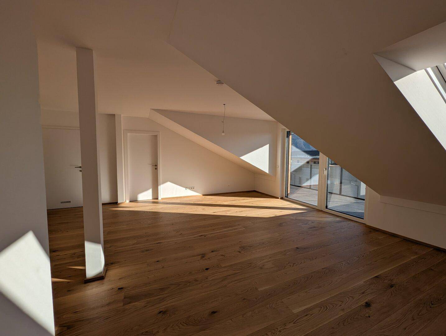 Heller Wohnraum im Dachgeschoss mit Eichenparkett, hohen Decken und Zugang zum Balkon.