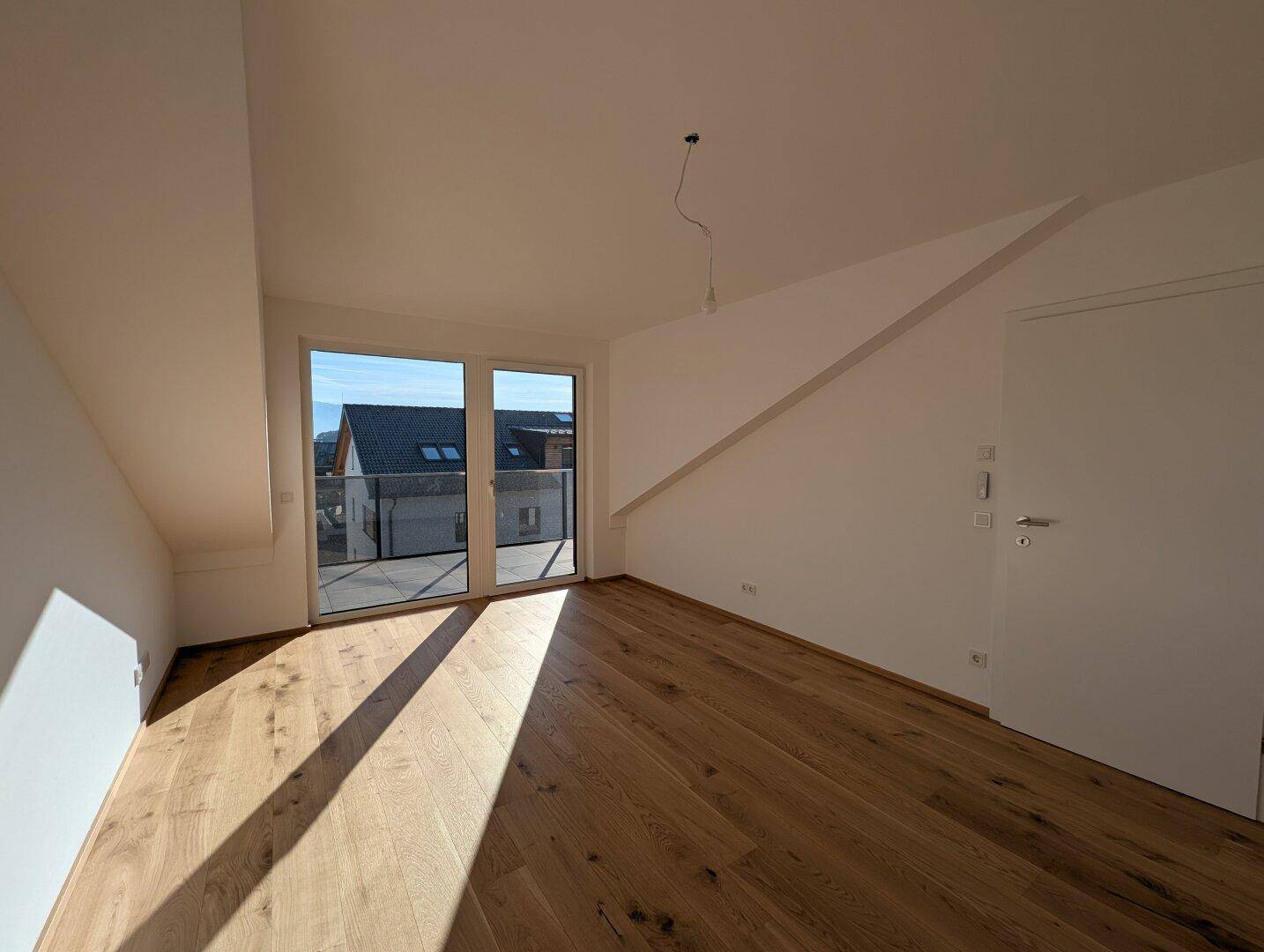 Heller Wohnraum mit Eichenparkett und großem Fenster, das Zugang zu einem französischen Balkon bietet.