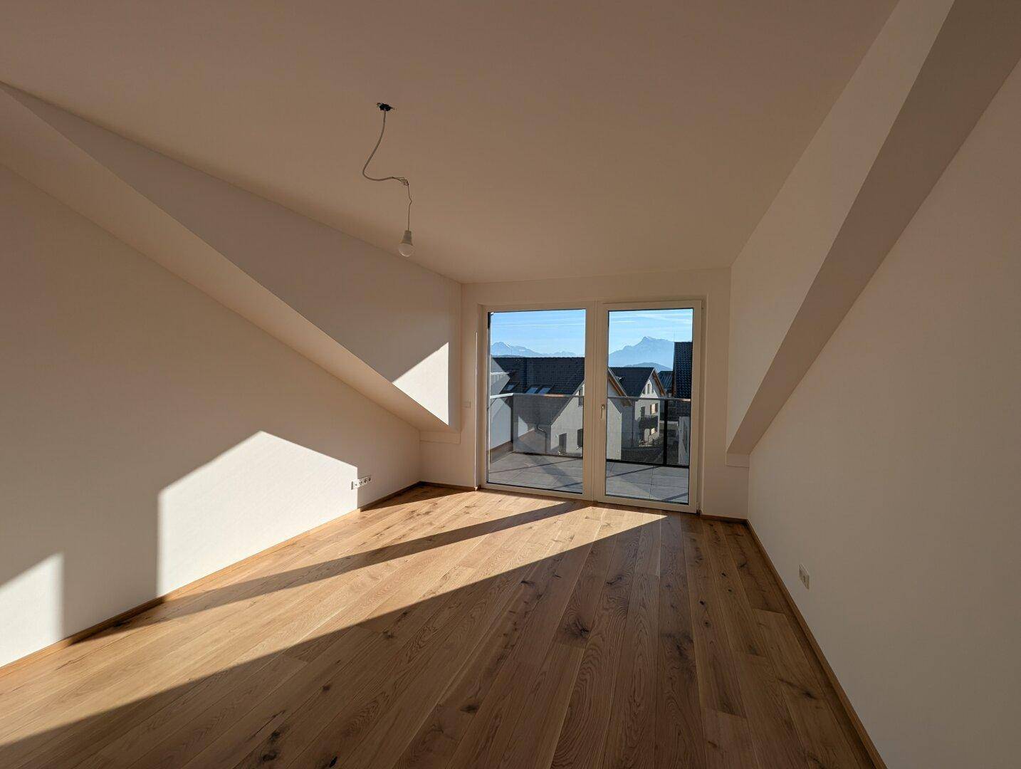 Lichtdurchfluteter Raum mit Holzboden und Zugang zu einem Balkon, ideal für ein Schlaf- oder Wohnzimmer.