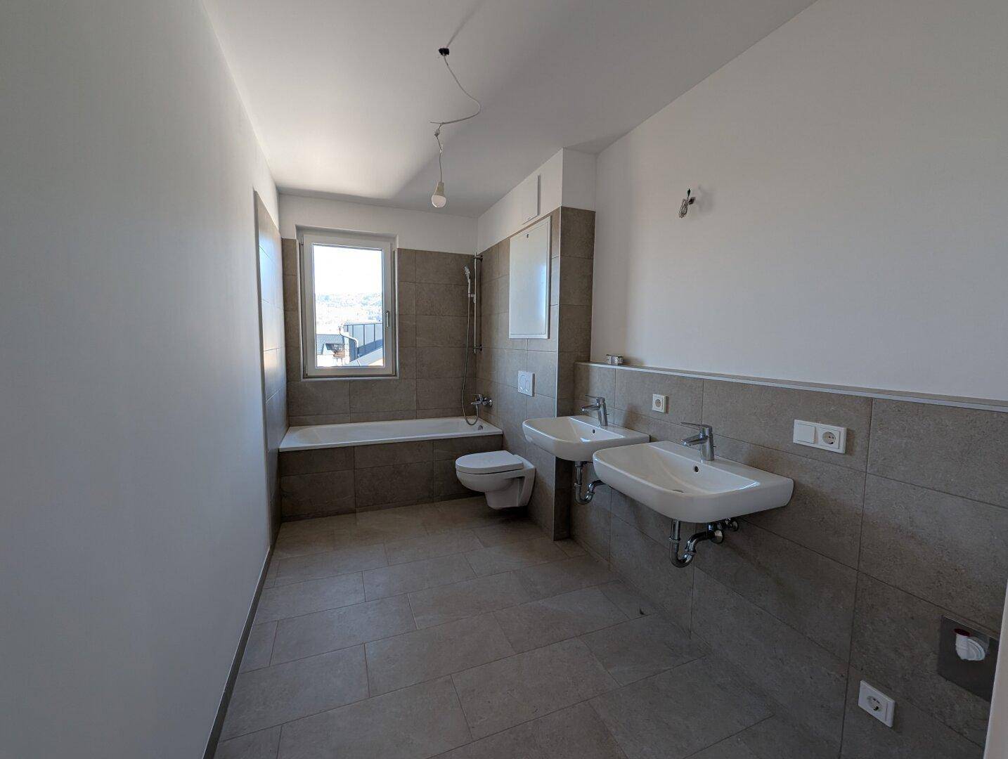 Modernes Badezimmer mit Doppelwaschbecken, Badewanne und Fliesenboden in neutralen Grautönen.