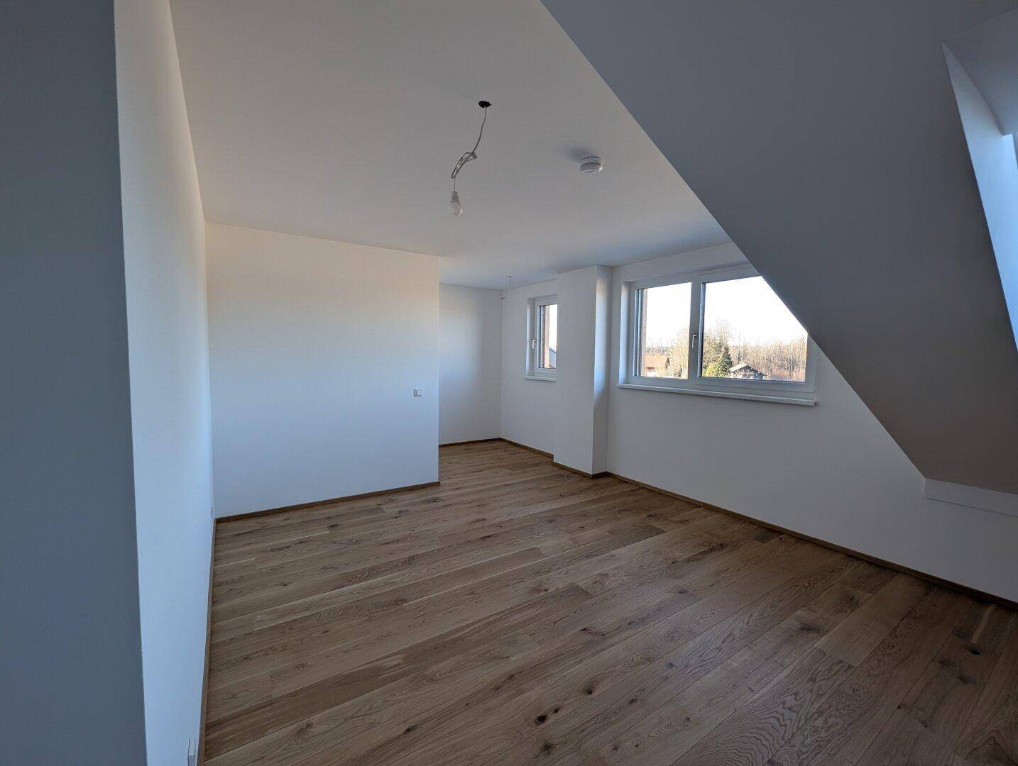 Helles Schlafzimmer mit Eichenparkett und zwei Fenstern, die einen weiten Blick ins Grüne ermöglichen.