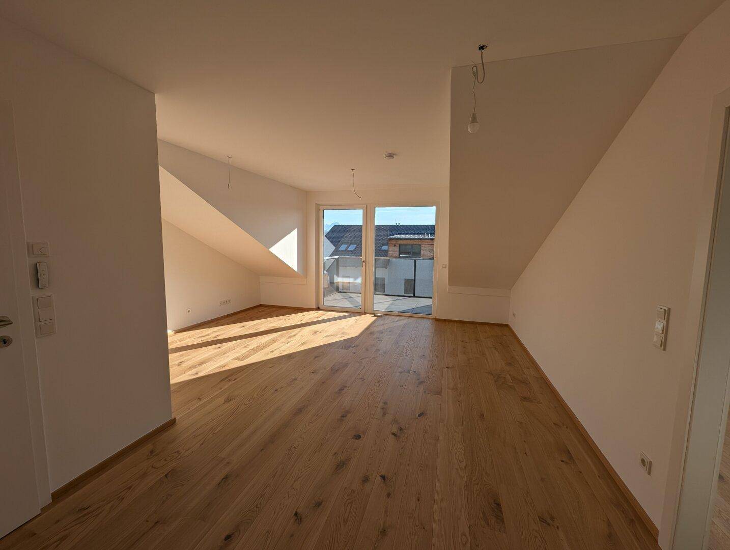 Geräumiger, heller Wohnbereich mit Holzboden und Zugang zu einem Balkon.