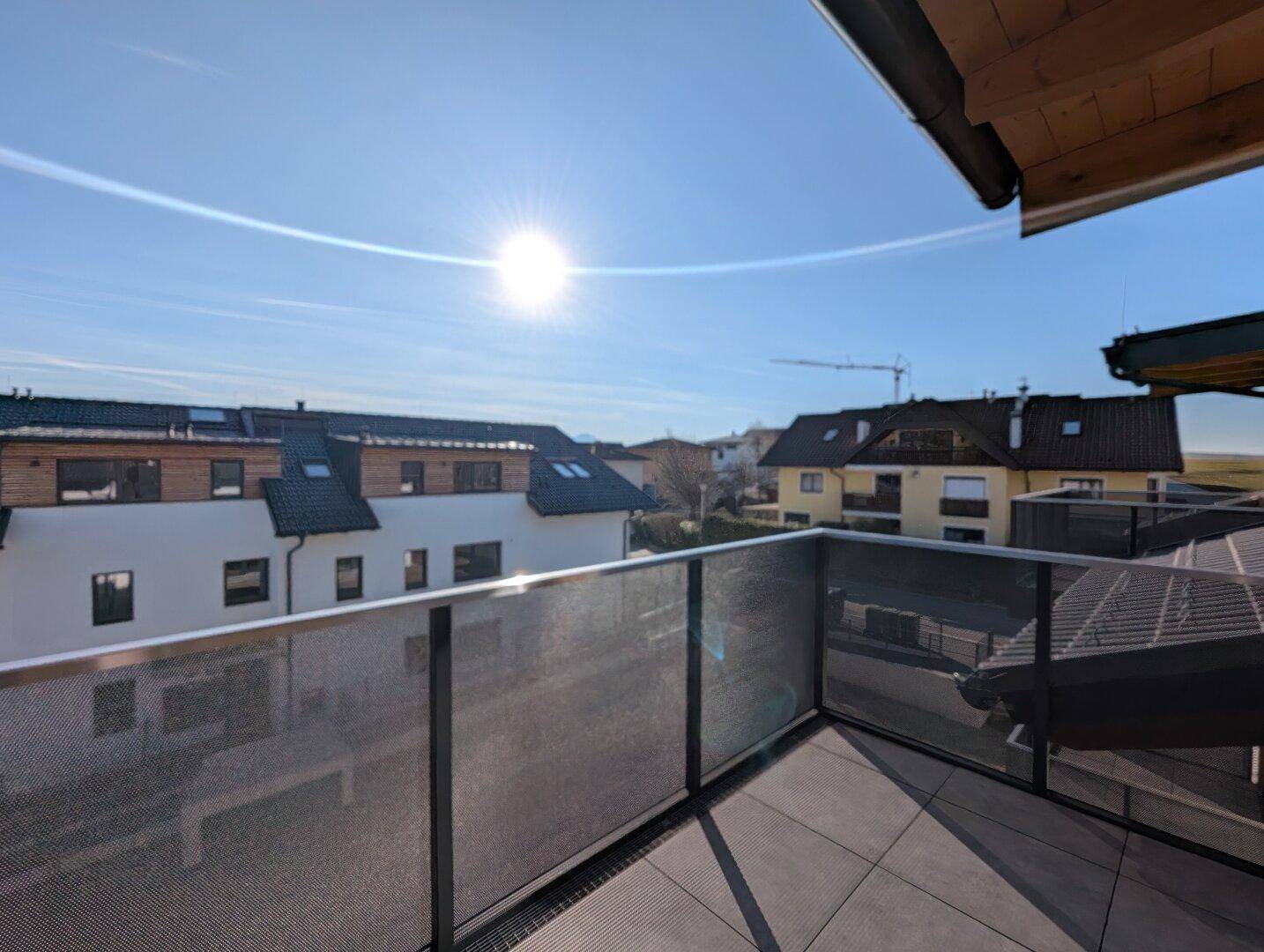 Sonniger Balkon mit Fliesenboden und Blick auf die umliegenden Häuser und den Himmel.