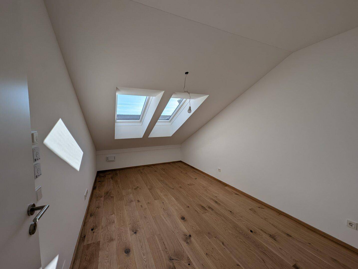 Helles Zimmer mit Holzboden und zwei Dachfenstern, ideal für Schlaf- oder Arbeitsbereich.