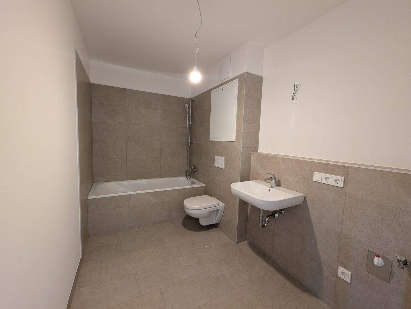 Modernes Badezimmer mit Badewanne, WC und Waschbecken, gefliest in neutralen Tönen.