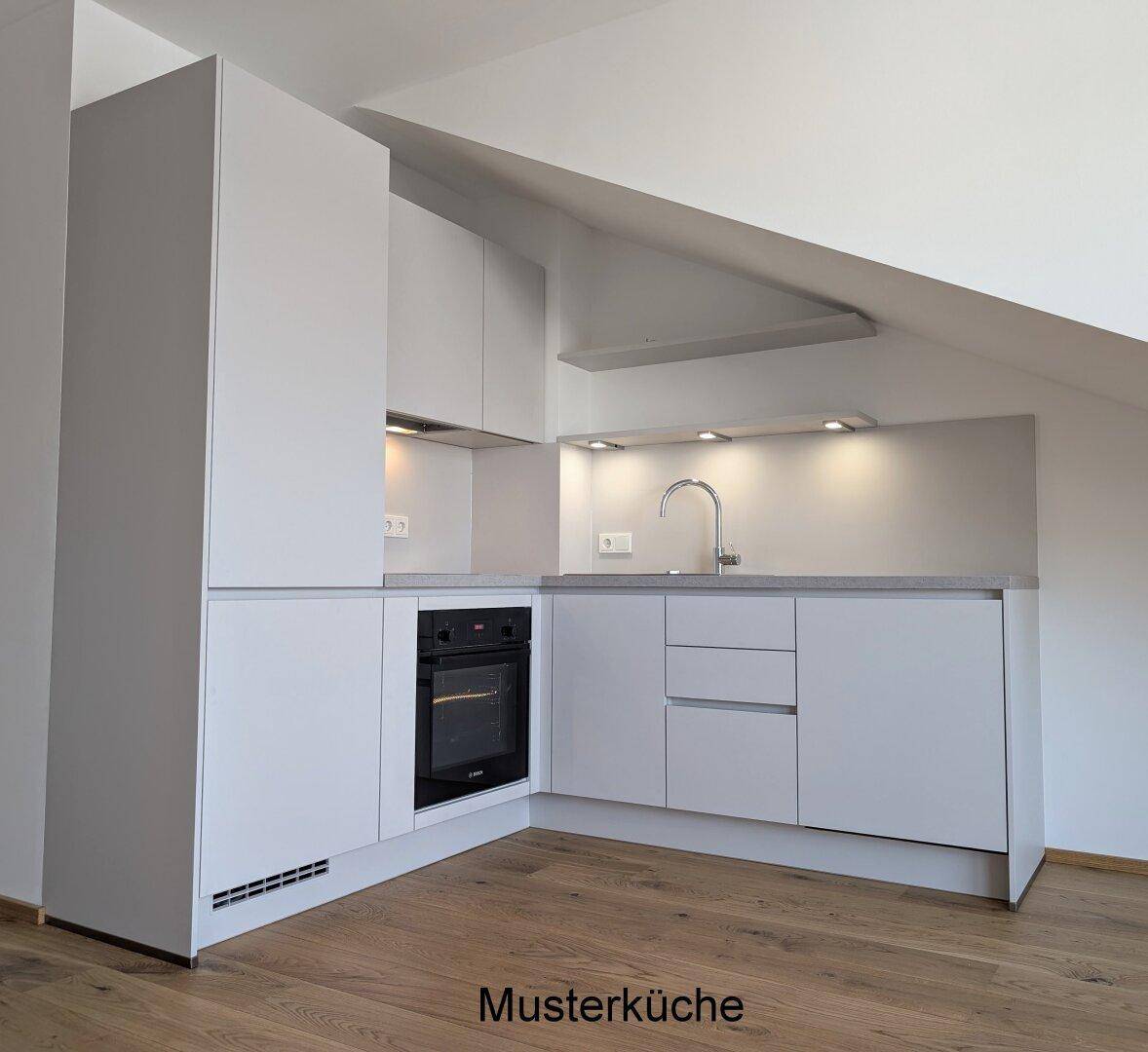 Moderne Einbauküche in Grau mit integriertem Backofen und Arbeitsplatte unter Dachschräge.