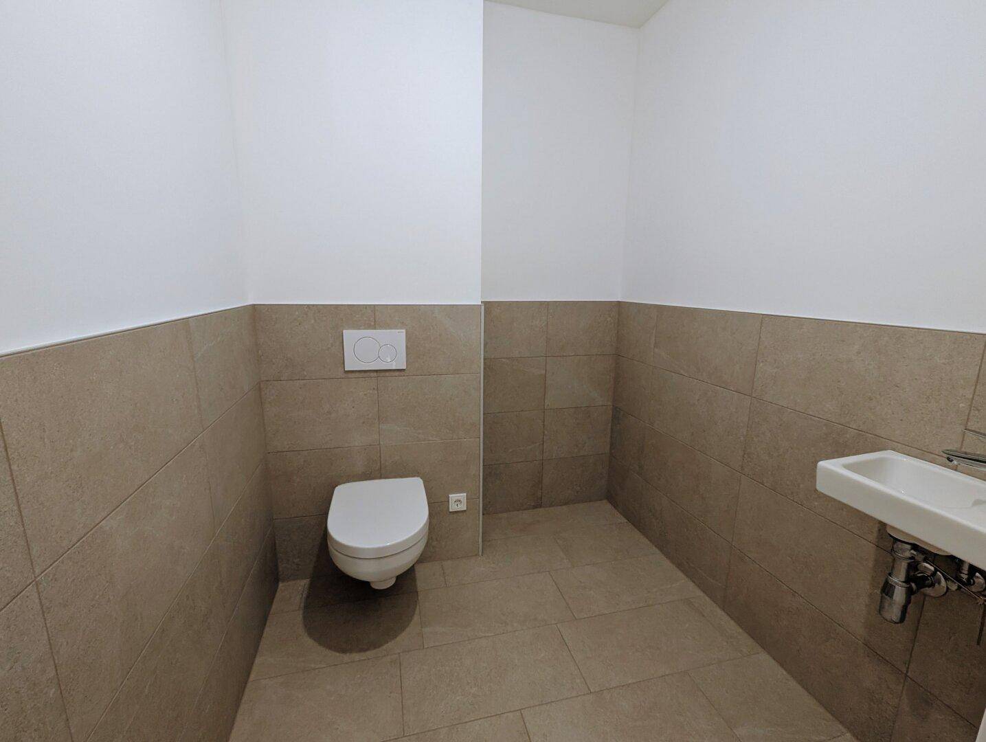 Praktisches Gäste-WC mit modernen grauen Fliesen, wandhängendem WC und einem kleinen Handwaschbecken.