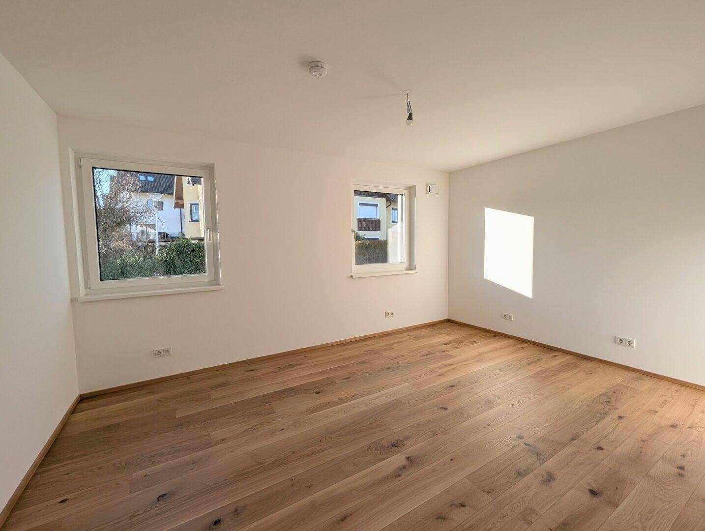 Helles Zimmer mit Eichenparkett und zwei Fenstern, die einen angenehmen Blick ins Grüne bieten.