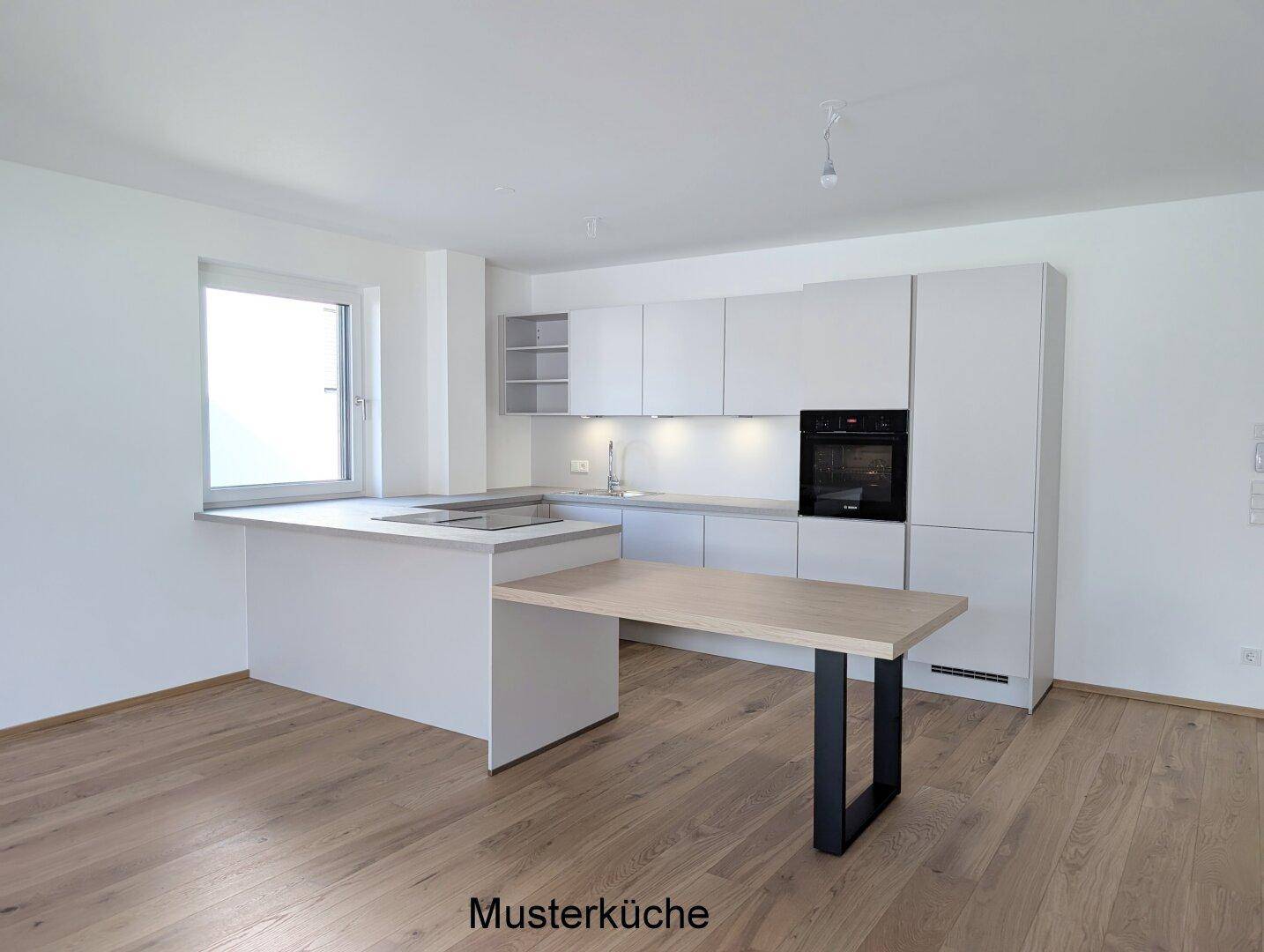 Moderne Musterküche mit hellgrauen Schränken, integriertem Backofen und Kochfeld, ergänzt durch einen Holztisch.