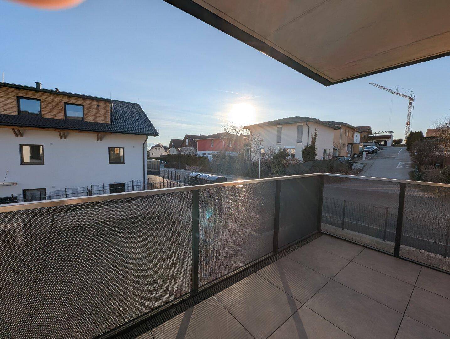 Sonniger Balkon mit Fliesenboden und moderner Brüstung, bietet einen Blick auf die Straße und umliegende Häuser.