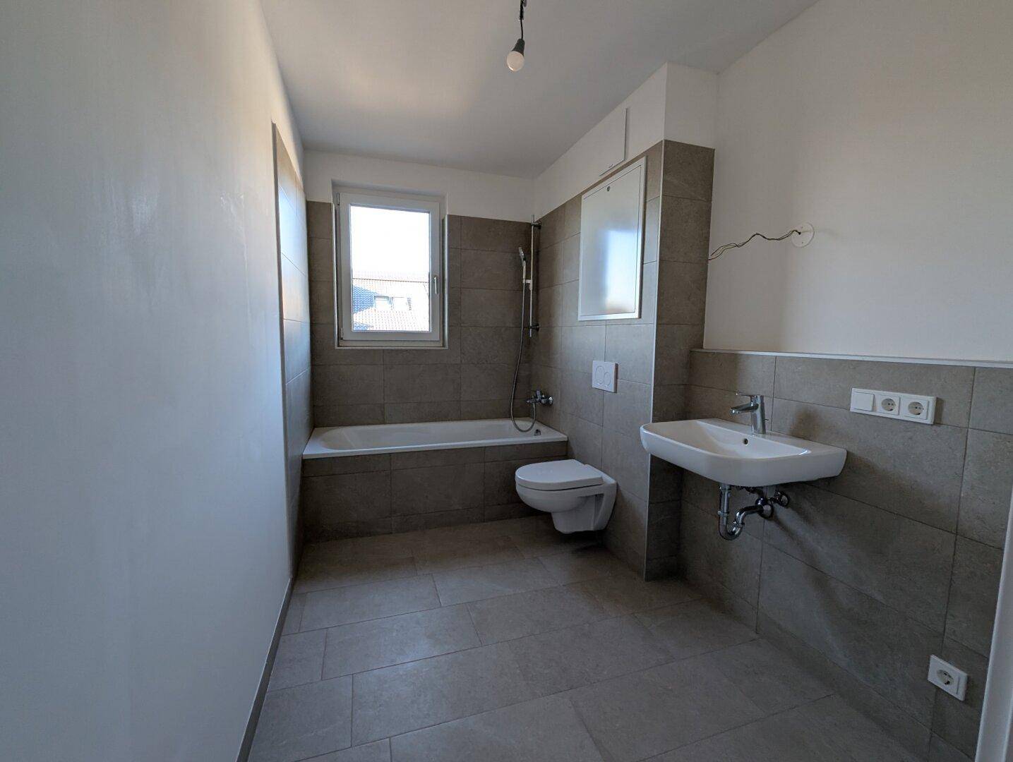 Modernes Badezimmer mit Badewanne, WC und Waschbecken, hell gefliest.