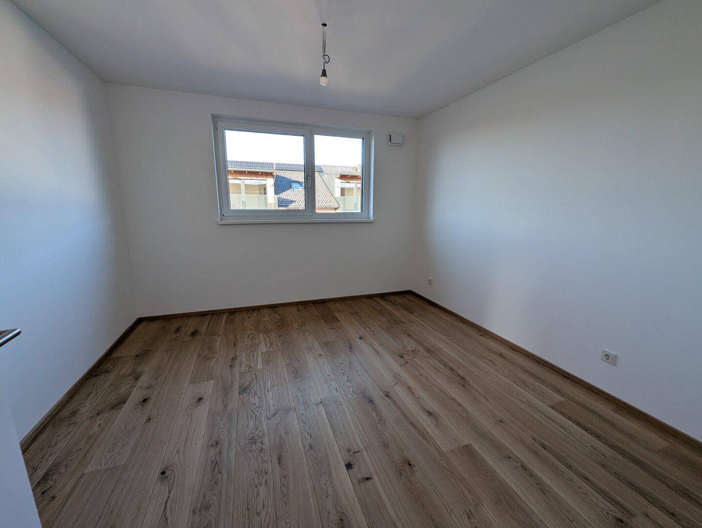 Freundliches Zimmer mit Holzboden und großem Fenster, bietet viel Tageslicht.