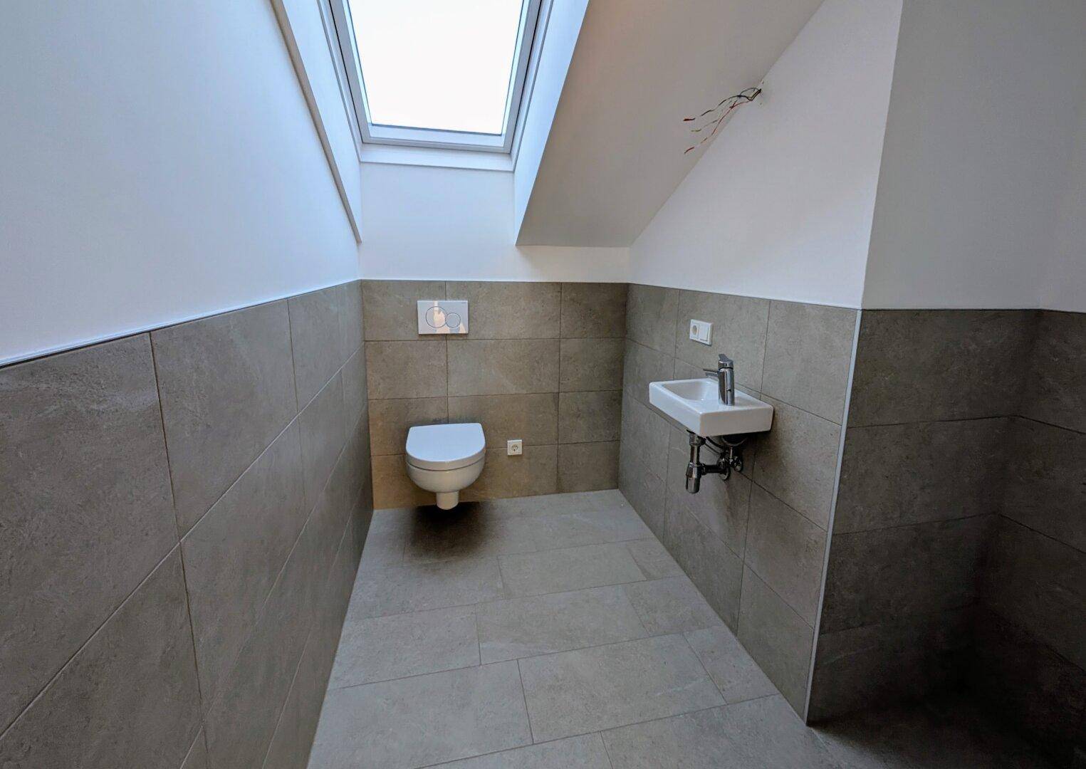 Separates WC im Dachgeschoss mit Waschbecken, Wand-WC und Dachfenster.