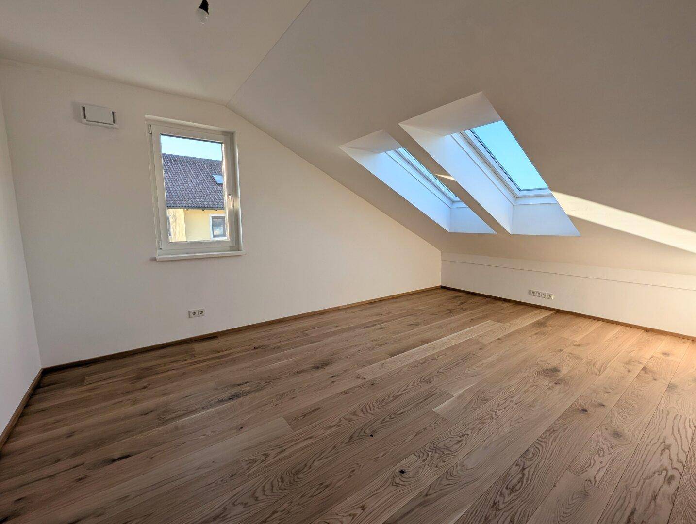 Lichtdurchflutetes Zimmer im Dachgeschoss mit Holzboden und zwei Dachfenstern.