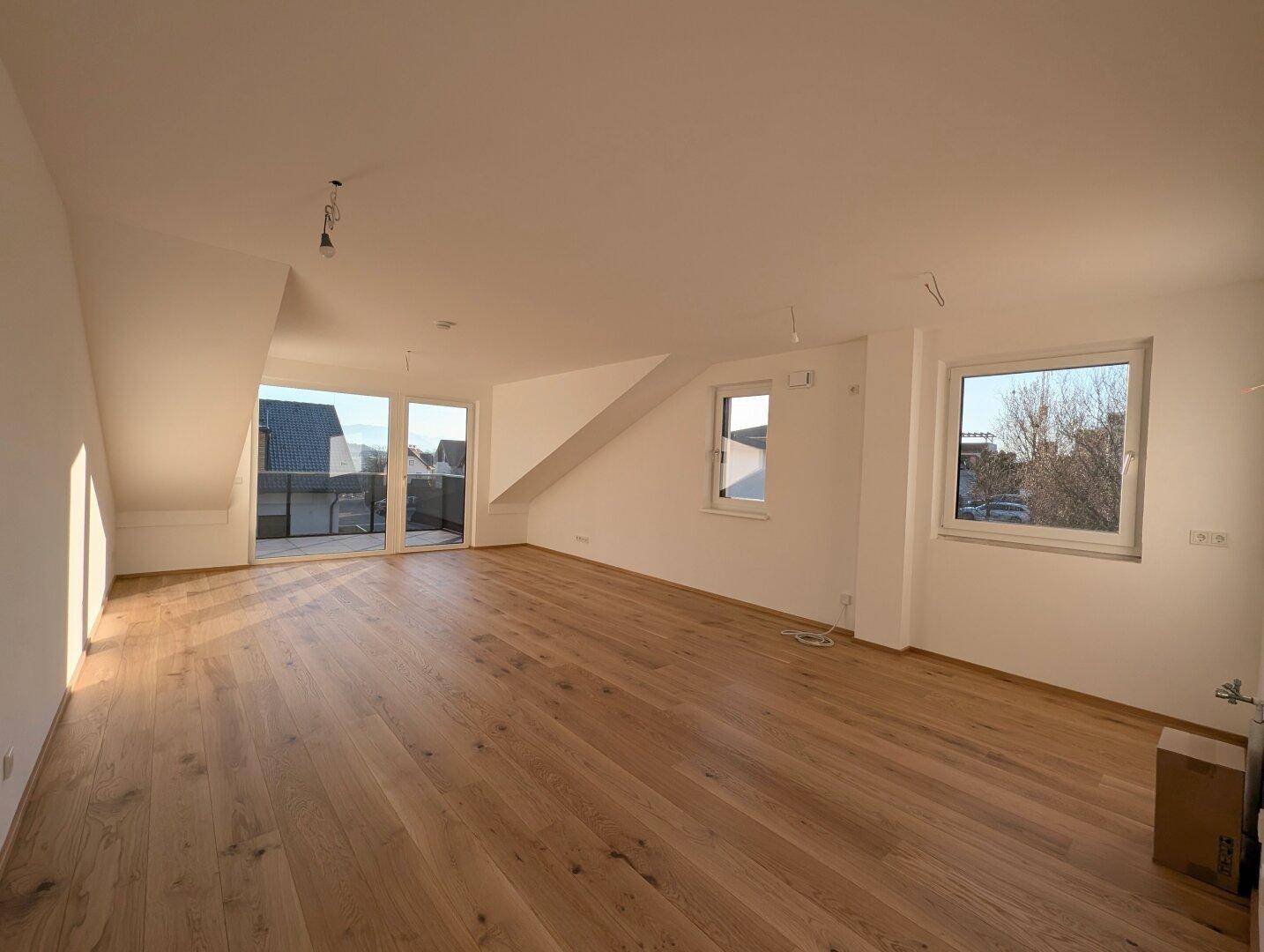 Geräumiger, heller Wohnbereich im Dachgeschoss mit Holzboden und Zugang zu einem Balkon.