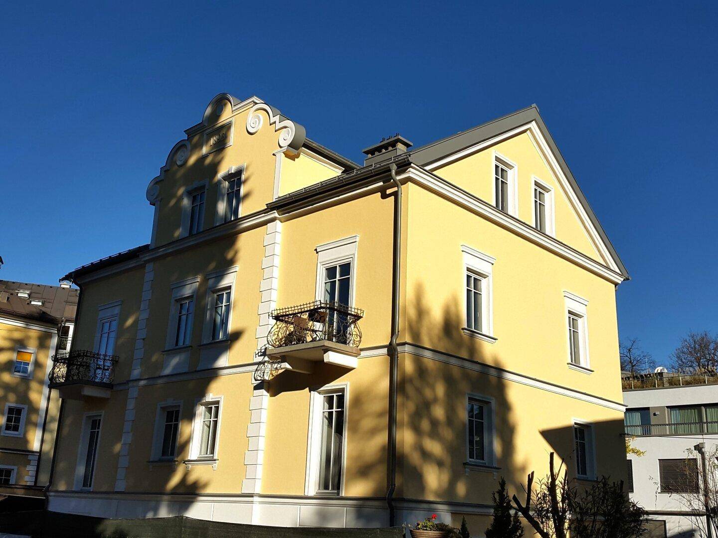 Seitenansicht des historischen Gebäudes mit gelber Fassade, Satteldach und sonniger Ausrichtung.