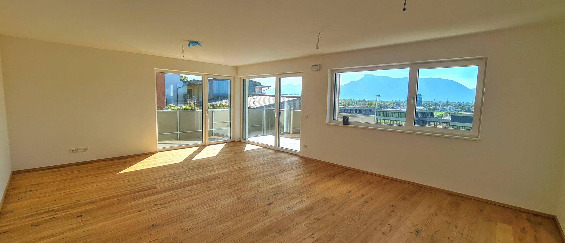Helles Wohnzimmer mit Holzboden, großen Fenstern und Zugang zu einem Balkon mit Bergblick.
