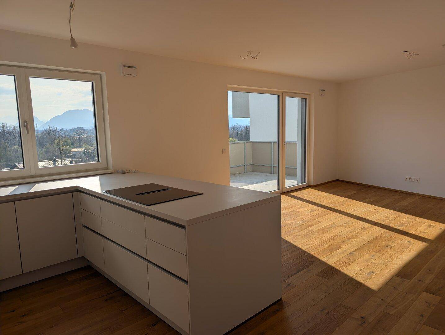 Offene Küche mit Kochinsel, Holzboden und großem Fenster mit Bergblick, angrenzend an den Wohnbereich.