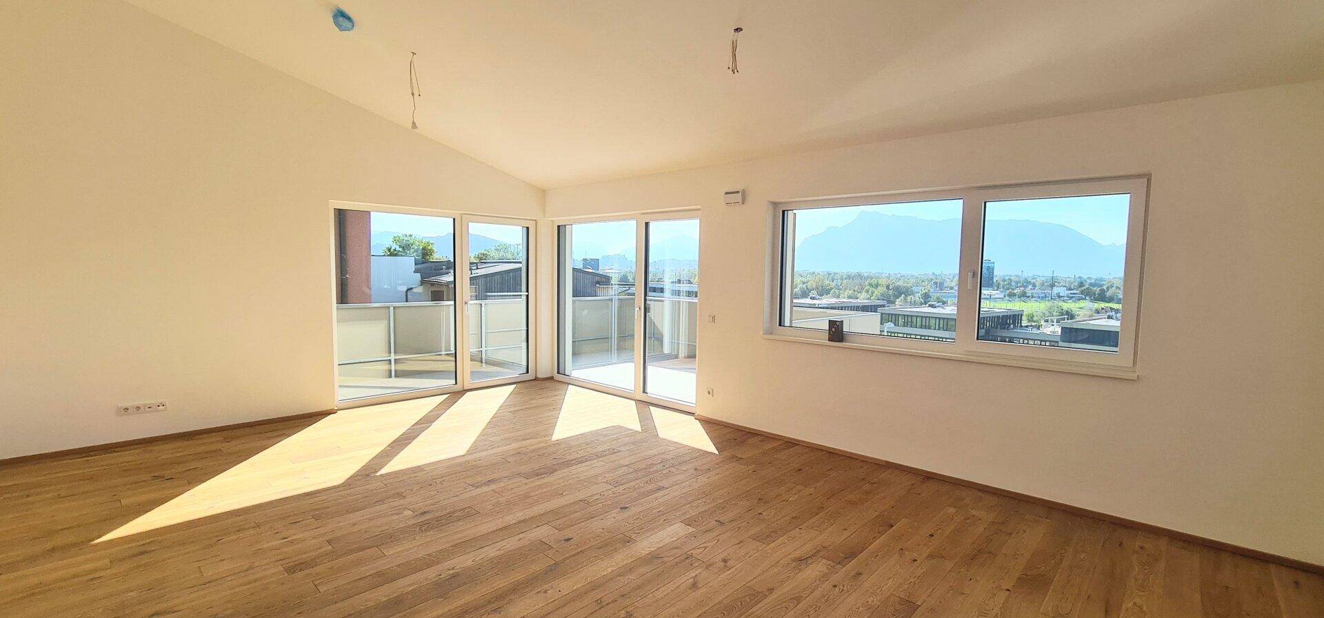 Lichtdurchflutetes Wohnzimmer mit Holzboden, großen Fenstern und Zugang zu einem sonnigen Balkon.